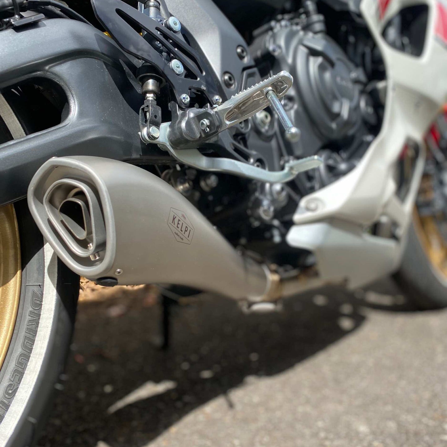 A stainless steel Alpha Muffler with a hydroformed shape, placed on a textured brown surface.