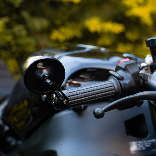 Close-up image of a Fitzroy grip with a black surface and open-end casting design, mounted on a motorcycle handlebar and a Hindsight bar end mirror