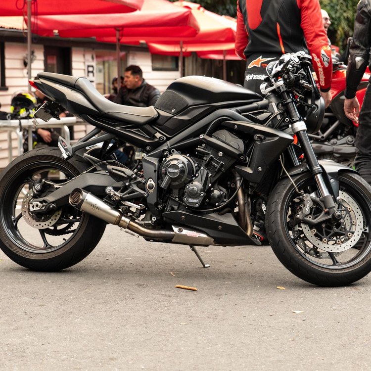 A carbon-fiber Kelpi Flanker muffler with a stainless steel shell, carbon fibre end cap, and a black mounting bracket on a Triumph Street Triple.