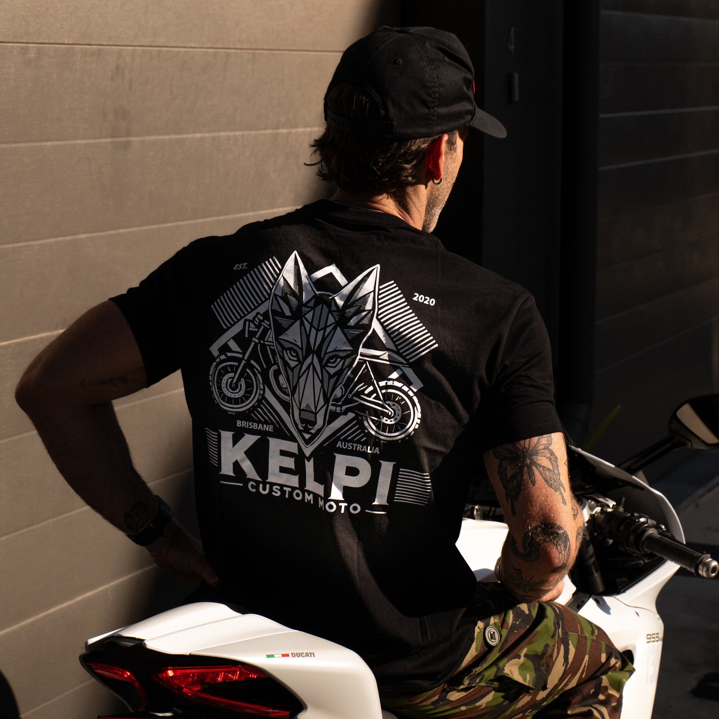 Person wearing a black Kelpie shirt sitting on a motorcycle.