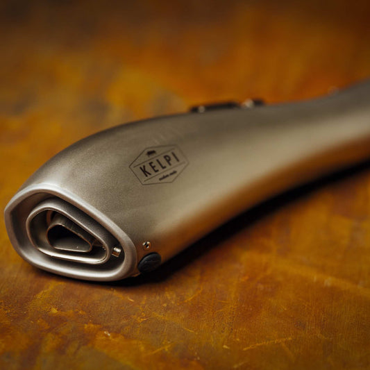 A stainless steel Alpha Muffler with a hydroformed shape, placed on a textured brown surface.