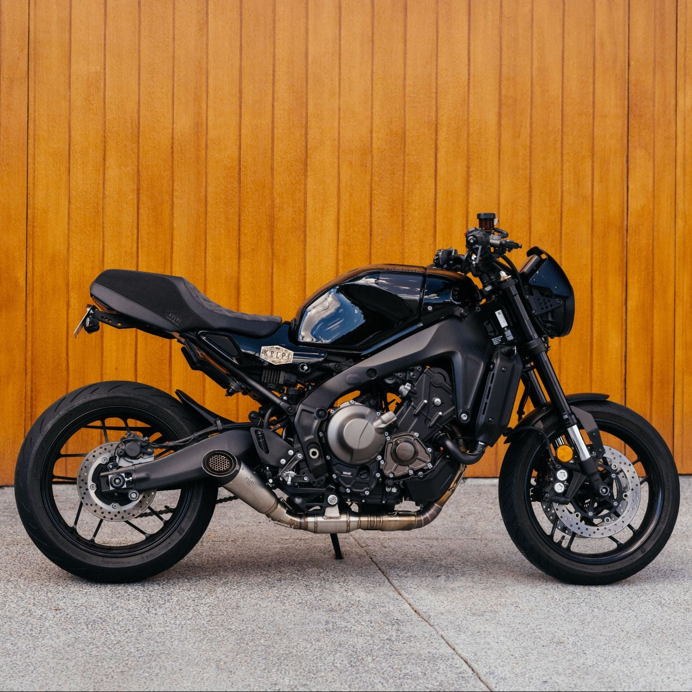 Black motorcycle parked against a wooden wall