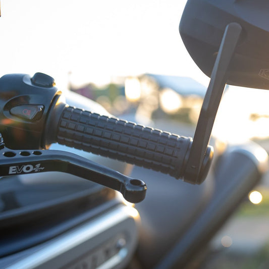 Close-up of motorcycle handlebar and mirror with blurred background.