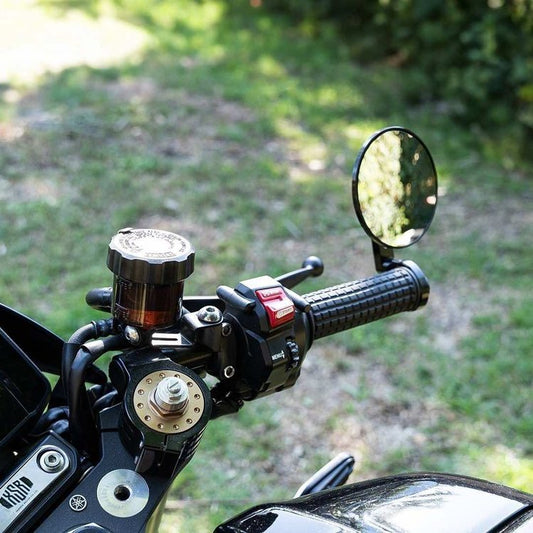 A black anodised machined billet alloy bar-end mirror mounted on a motorcycle handlebar, with a mirror ball joint and adjustment dials visible.