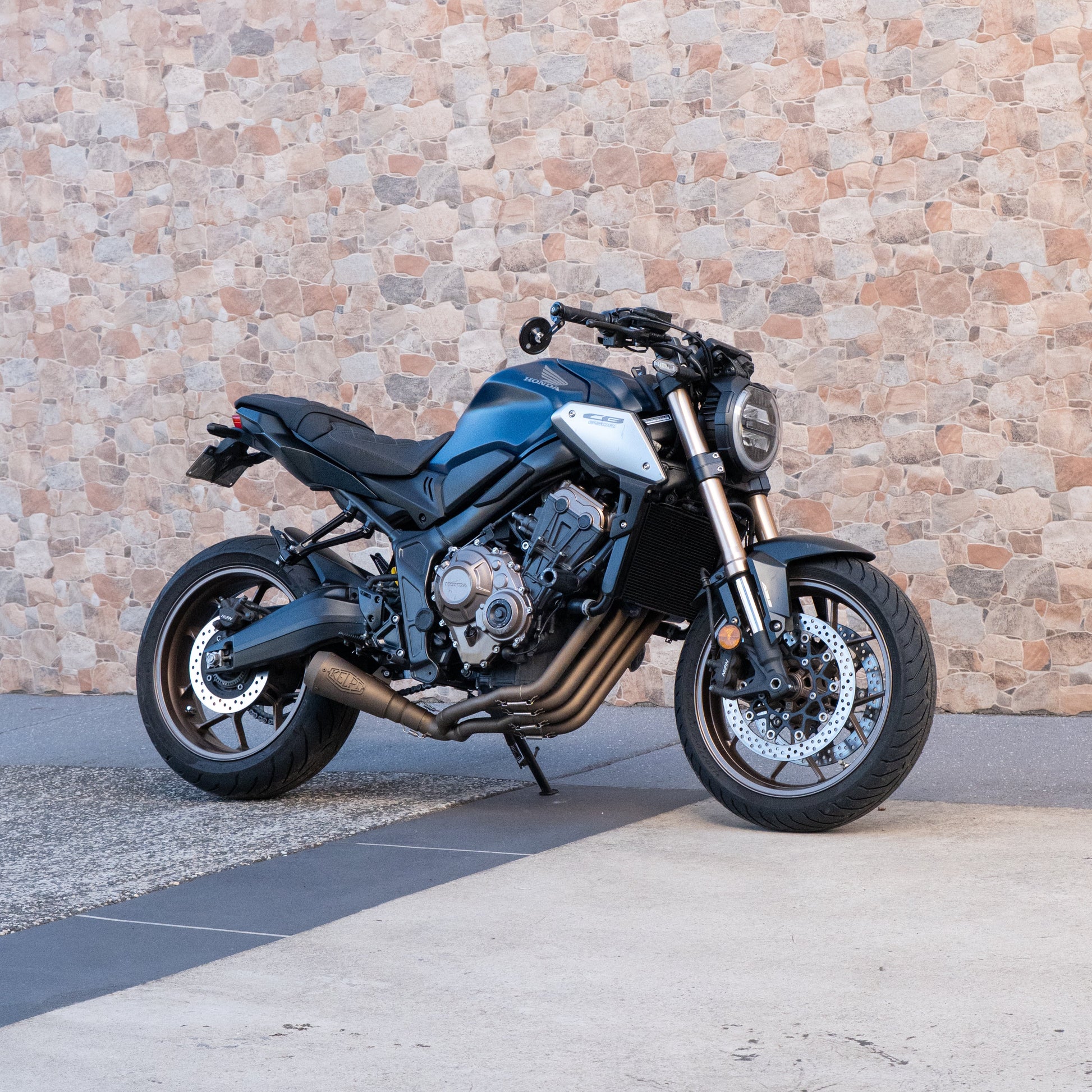 Blue motorcycle parked on a concrete surface with a brick wall in the background