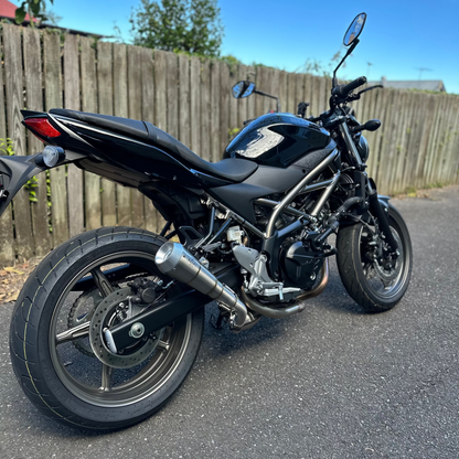 Black motorcycle parked on a paved surface with a wooden fence and trees in the background.