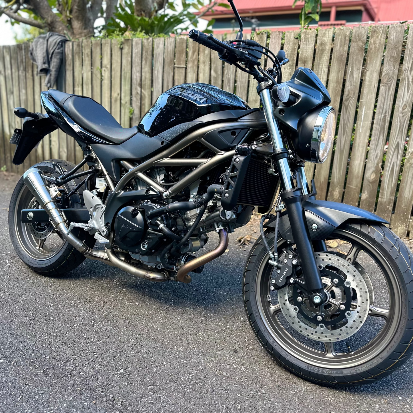 Black motorcycle parked on a street with a wooden fence in the background