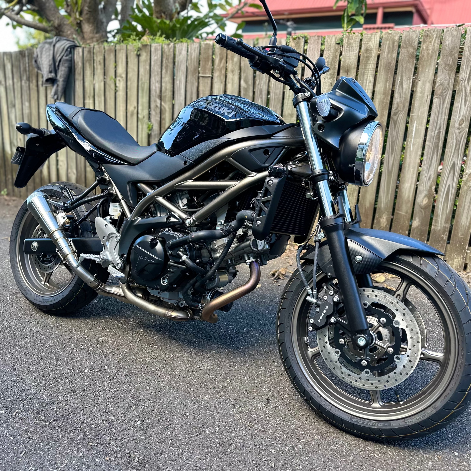 Black motorcycle parked on a street with a wooden fence in the background