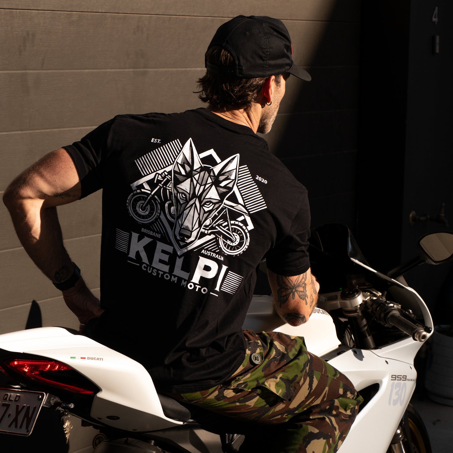 Person wearing a black t-shirt with a logo and text, sitting on a white motorcycle.