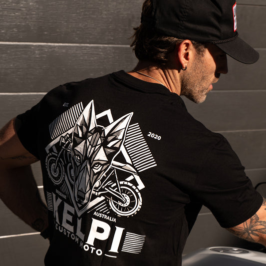 Person wearing a black t-shirt with a motorcycle graphic and 'KELPI' branding, sitting on a motorcycle.